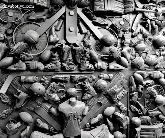 A complex arrangement of various sports equipment and attire, including tennis rackets, soccer balls, basketballs, helmets, shoes, gloves, and a mannequin torso wearing a T-shirt. The items are layered and artistically displayed in a monochrome color scheme, creating an intricate texture and visual pattern.